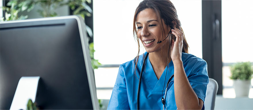 A nurse sitting at a computer on a phone with a headset on, standing by to take your call